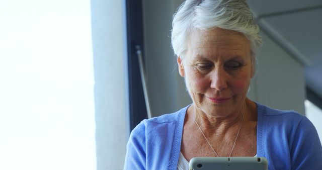 A senior Caucasian woman is focused on her tablet, with copy space. Her engagement with technology reflects the increasing digital literacy among older generations.