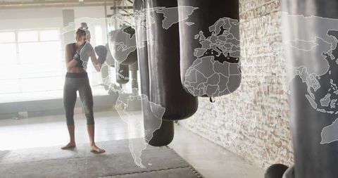 Female boxer training on heavy bag in loft gym with global map overlay, fitness concept