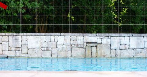 Backyard pool with rippling blue water by stone retaining wall and lush green treeline