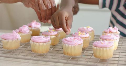 African American grandma and granddaughter decorating pink frosted cupcakes