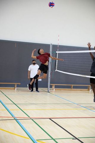 Teen volleyball player jumping to spike ball in indoor court with coach watching