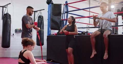 Diverse boxing team wrapping hands by ring preparing for training and sparring