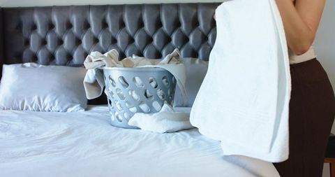Folding towels on bed with laundry basket and tufted headboard