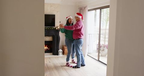 Couple Dancing Cheerfully Wearing Santa Hats at Home during Holidays