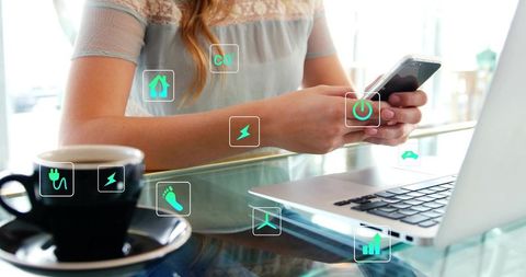 Woman using smartphone and laptop in sunlit cafe with floating energy app icons