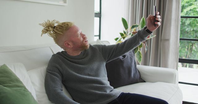 Albino african american man with dreadlocks using smartphone. leisure time, using technology, relaxing at home.
