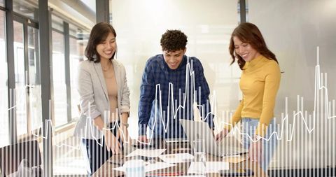 Young professionals collaborating around laptop and printed charts in modern glass office