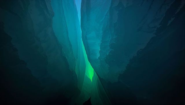 Emerald crevice glowing upward in narrow canyon with layered teal rock and luminous haze