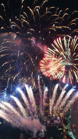 Vertical fireworks display lighting downtown skyline, bursting red and blue over rooftops