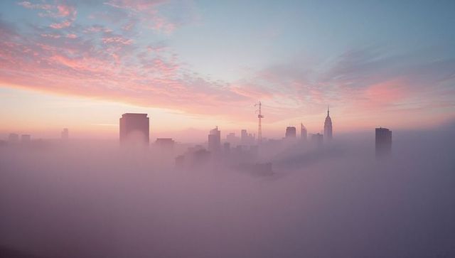 Fog-Piercing Skyscrapers at Pastel Sunrise Over Urban Landscape