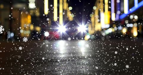 Nighttime city street with falling snowflakes, wet pavement and headlight glare