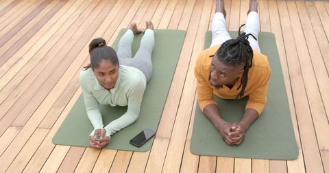 Diverse Couple Practicing Plank on Green Yoga Mats on Wooden Deck During Outdoor Workout