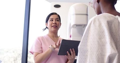 Radiology Technologist Explaining Mammogram Using Tablet While Preparing Patient for Breast Screenin