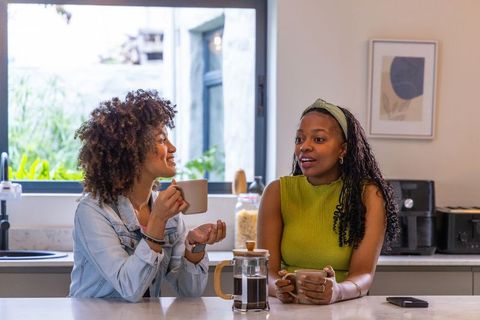 African american women chatting and smiling over coffee in bright modern kitchen