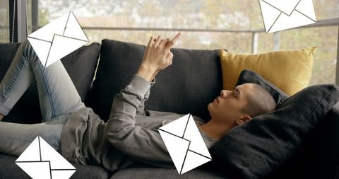 Young Man Relaxing on Couch Using Smartphone with Digital Envelopes