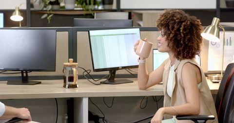 Professional Woman Drinking Coffee Analyzing Reports in Modern Office