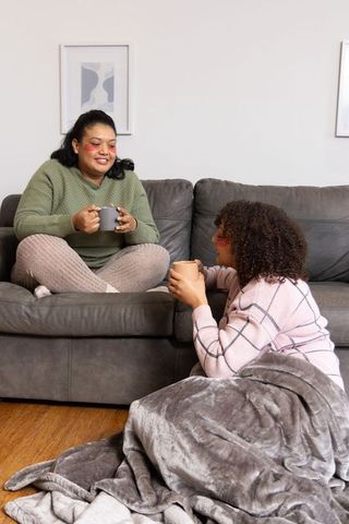 African american women sharing cozy coffee and conversation on gray living room sofa