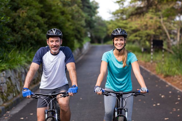 Couple cycling on a scenic open road, both smiling and wearing helmets. Perfect for promoting fitness, active lifestyle, outdoor sports, and healthy living campaigns.