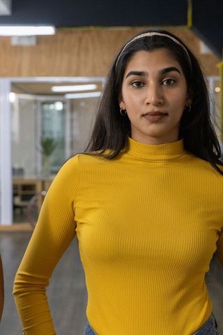Confident indian woman standing in coworking office wearing mustard ribbed turtleneck