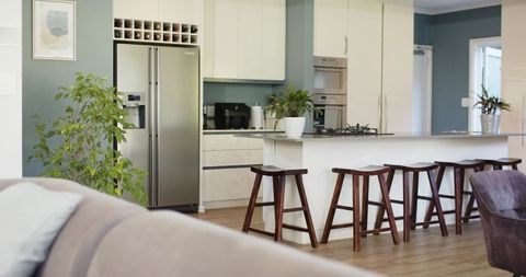 Modern open-plan kitchen featuring island with wooden bar stools, stainless refrigerator