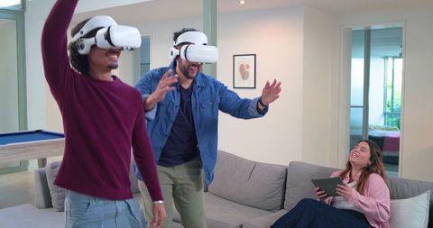 Friends playing virtual reality games in modern living room with tablet and laughter