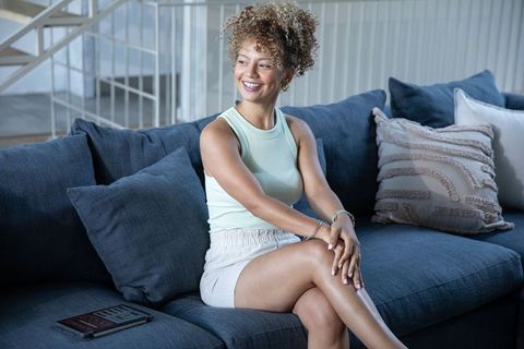 Smiling african american woman relaxing on blue sofa in modern living room