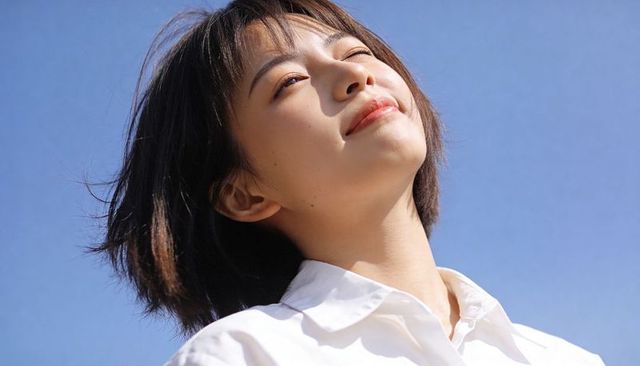 Short-haired woman tilting face toward sun smiling under clear blue sky
