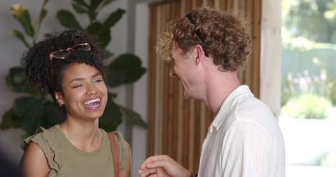 Couple greeting and laughing in sunlit entryway with houseplant and garden view