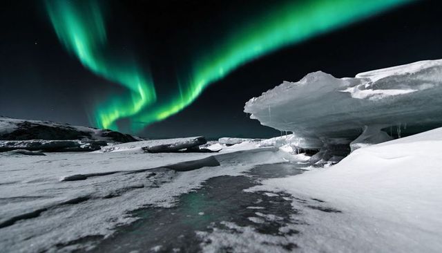 Glowing green aurora stretching over icy arctic tundra under starry night
