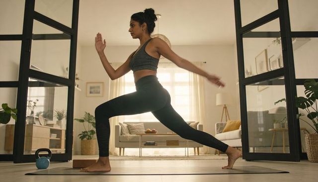 Indian woman practicing yoga lunge in minimalist living room for home fitness and wellness