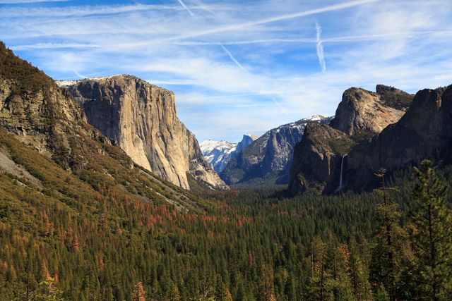 Captivating image showcasing Yosemite Valley with its vast pine forests cloaked between towering snow-capped mountains and clear blue sky. Ideal for travel magazines, nature documentaries, eco-awareness campaigns, and outdoor adventure promotions.