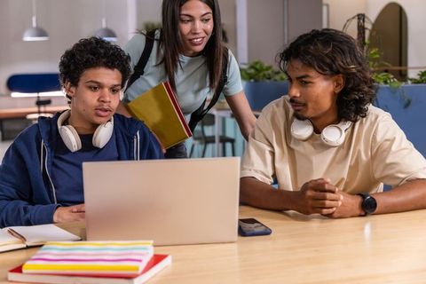 Diverse students collaborating and studying around laptop in modern campus lounge