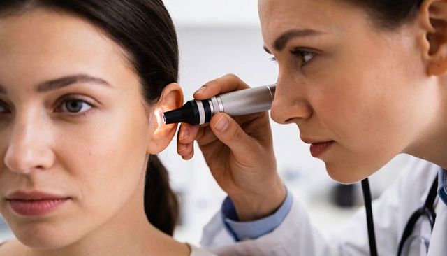 Doctor examining female patient ear with otoscope during clinic checkup, closeup