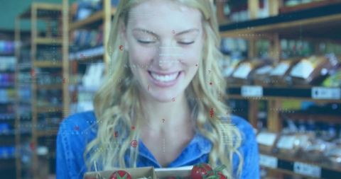 Smiling woman holding crate of ripe tomatoes in grocery aisle with digital data overlays