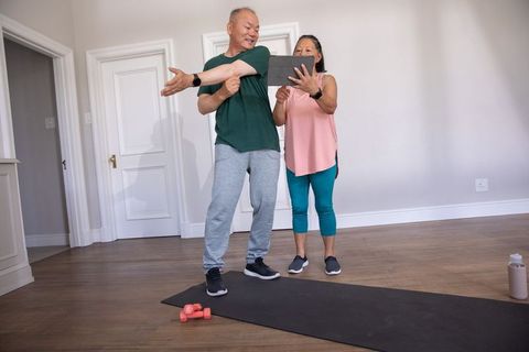Senior chinese couple stretching and following online workout on tablet at home gym