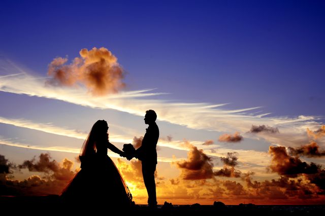 The image shows a romantic couple holding hands at sunset on a beach with a vibrant sky, and the couple's silhouettes add a dramatic effect. Perfect for use in wedding-related content, romantic announcements, and travel ads focused on beach destinations.