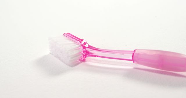 A pink toothbrush lies on a white background, with copy space. Its simplicity emphasizes the importance of daily oral hygiene.