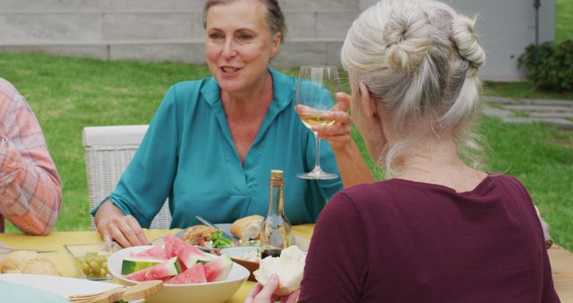 Image of happy caucasian senior woman eating lunch in garden with friends. retirement lifestyle, spending quality time with friends.