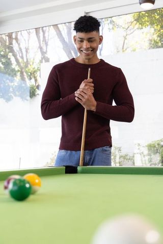African american man smiling and playing pool in bright modern home lounge