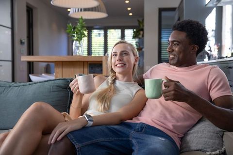 Diverse couple enjoying coffee on comfortable teal sofa