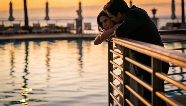 Romantic couple leaning on pool railing sharing golden hour gaze at waterfront resort