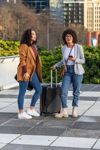 Two african american women traveling with suitcase in city plaza, casual business travel