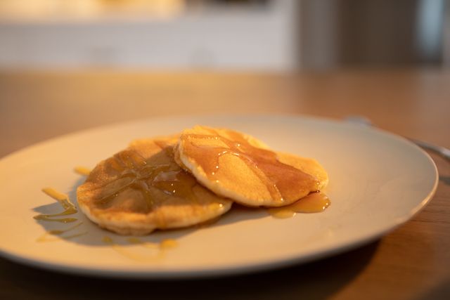 This image shows a close-up of two pancakes covered in maple syrup on a plate, placed on a wooden table. Ideal for use in food blogs, breakfast menus, recipe websites, or advertisements for breakfast products.