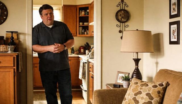 Man standing in doorway surveying cozy living room and compact kitchen with wood cabinets