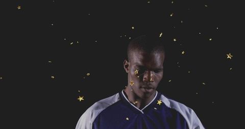 Standing man gazing down wearing blue white jersey with gold stars on dark backdrop