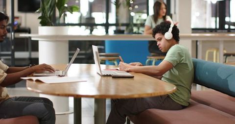 African American Student Writing Notes with Headphones in Bright Coworking Space