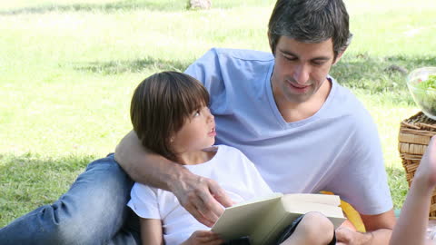 Father and Son Enjoy Reading Together During Picnic in Park