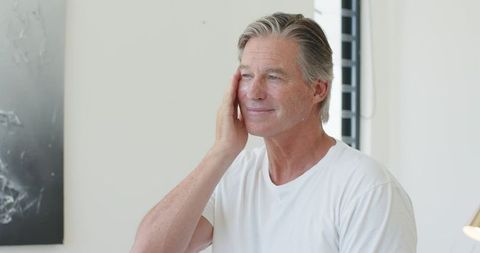 Mature man touching face in minimalist interior conveying calm skincare routine and wellness