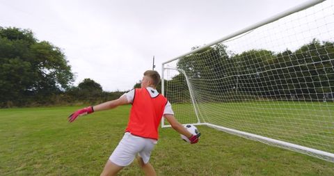 Teenager in red training vest playfully tossing soccer ball near goal