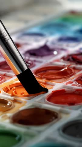 Vertical video capturing paintbrush dipping into orange watercolor well and forming droplet